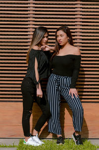 Full length of fashionable women standing against blinds