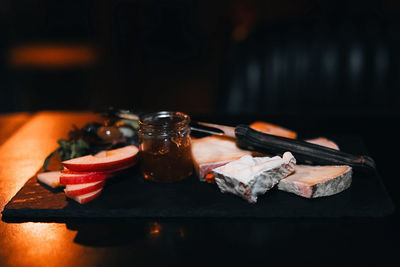 Composition of sliced cheese, a jar of honey and pieces of apples on a wooden stand