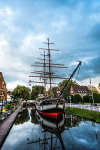 Sailboats moored on canal in city against sky