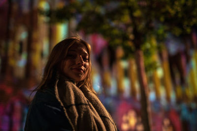 Portrait of smiling young woman standing outdoors at night