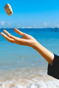 Close-up of woman throwing stone on beach against sky