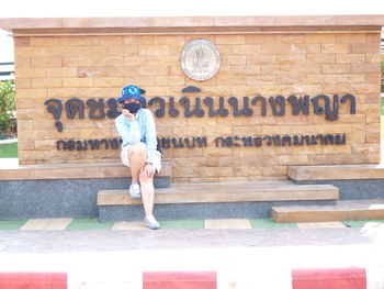 Full length of man sitting on bench against wall