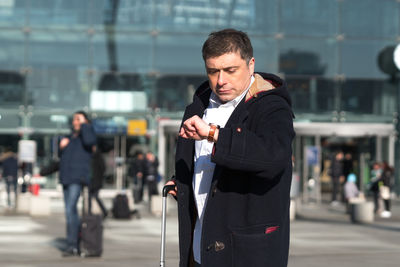 Man checking time while standing against building