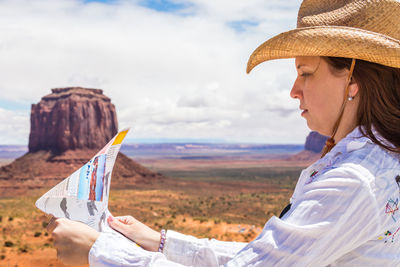 Portrait of woman holding hat against sky