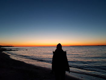 Rear view of silhouette woman sitting on beach at sunset