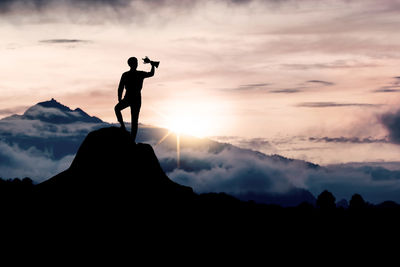 Silhouette man standing on rock against sky during sunset