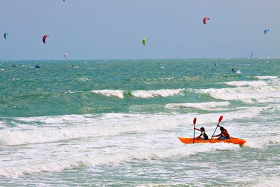 Men rowing boat on sea against clear sky