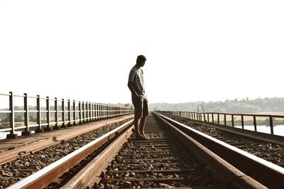 Rear view of man standing on railroad tracks against clear sky