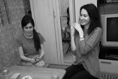 Smiling friends playing cards while sitting on table at home