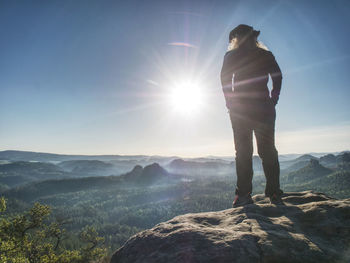 Hiker girl with leather cap with hands in pocket on cliff edge above misty valley. marvelous autumn