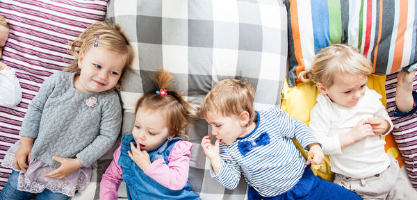 High angle view of cute kids lying down on bed at home