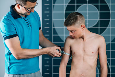 Man measuring shirtless male athlete bicep in health club