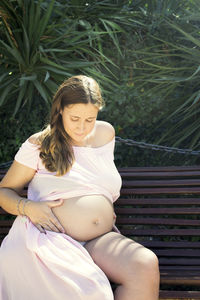 Seven months pregnant woman sitting on a wooden bench. very happy expression