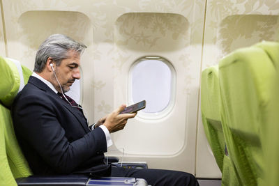 Side view of man wearing headphones sitting in airplane