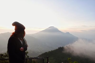 Rear view of man standing against mountain during sunset