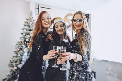 Portrait of smiling young women holding wineglasses against christmas tree