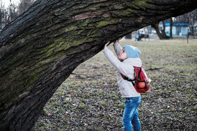 Side view of boy touching tree trunk at park