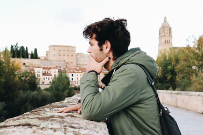 Side view of young man sitting on retaining wall