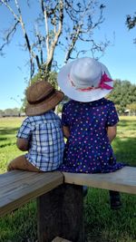 Rear view of children sitting on bench against sky