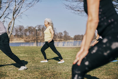 Senior people learning from female instructor while stretching at field