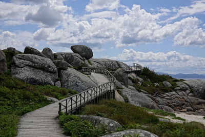 Walkway leading towards rocks against sky