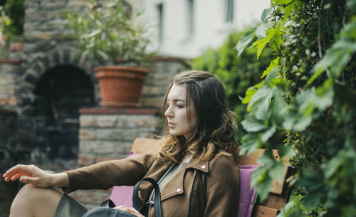 Thoughtful young woman sitting on bench by plant