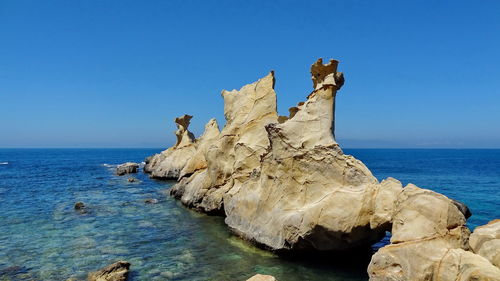 Rock formations in sea against clear blue sky