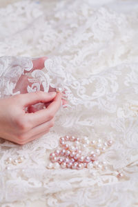 Cropped hand of woman stitching pearls on white wedding dress