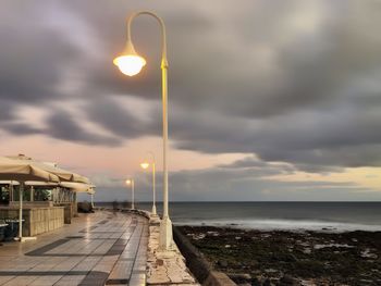 Street light on beach against sky during sunset