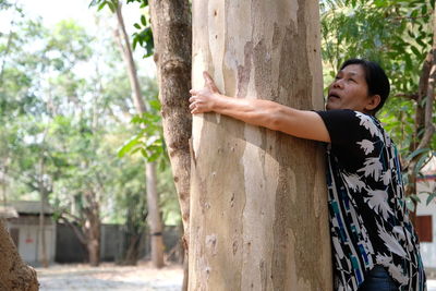 Side view of mature woman embracing tree trunk in forest