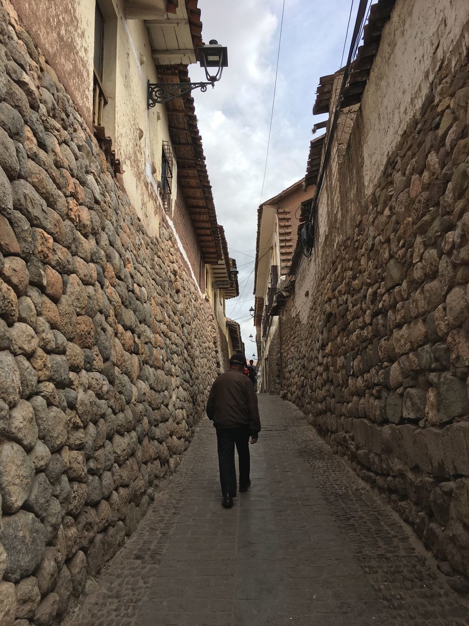 FULL LENGTH REAR VIEW OF WOMAN WALKING ON FOOTPATH AMIDST BUILDINGS