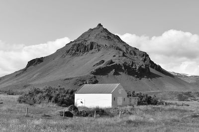 House on field by mountain against sky
