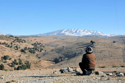 Rear view of man sitting on land against clear sky