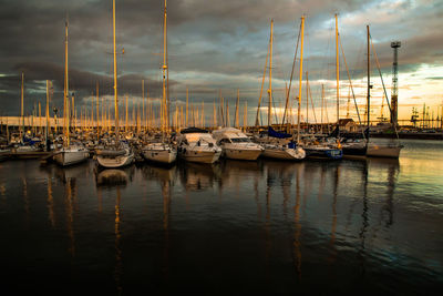 Sailboats moored in harbor at sunset