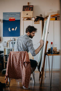 Rear view of man painting on canvas at home