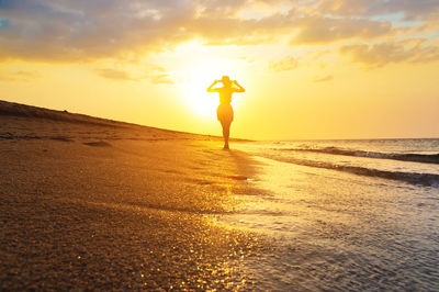 Silhouette woman walking at beach against sky during sunset