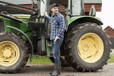 Full length of farmer standing by tractor on farm