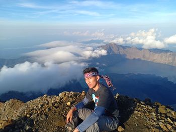 Man sitting on mountain against sky