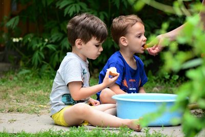 Cropped hand of mother feeding fruits to son sitting on land