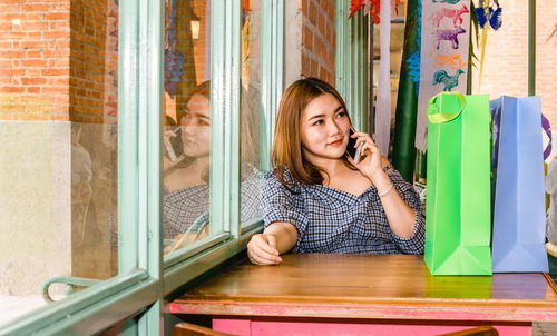 Portrait of a smiling young woman using phone on table