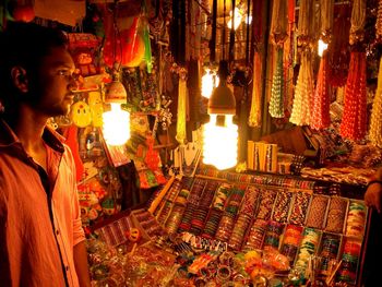 Bangle seller standing by illuminated market stall at night