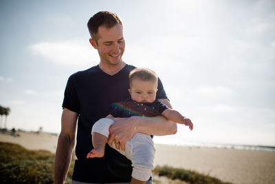 Father smiling & casually holding son on beach