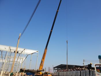 Low angle view of cranes against clear blue sky