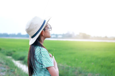 Side view of young woman wearing hat standing on field