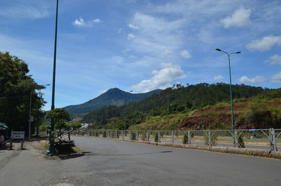 Empty road along trees and mountains against sky