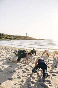 Male and female teammates exercising on sand during group training session at beach