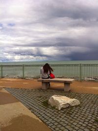 Rear view of people walking on pathway by river against cloudy sky