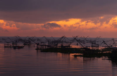 Silhouette cranes against sky at sunset