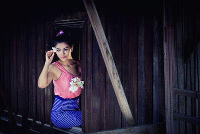 Portrait of young woman showing white flower on window