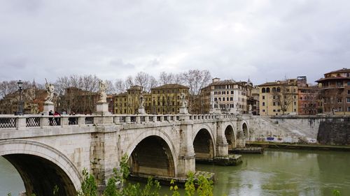 Arch bridge over river against cloudy sky